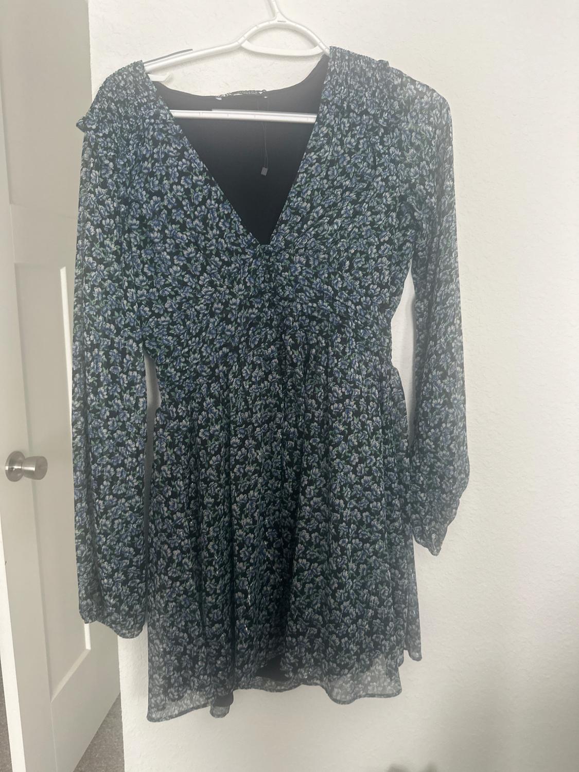 Blue and black floral print long-sleeved dress, hanging on a white hanger over a white door.