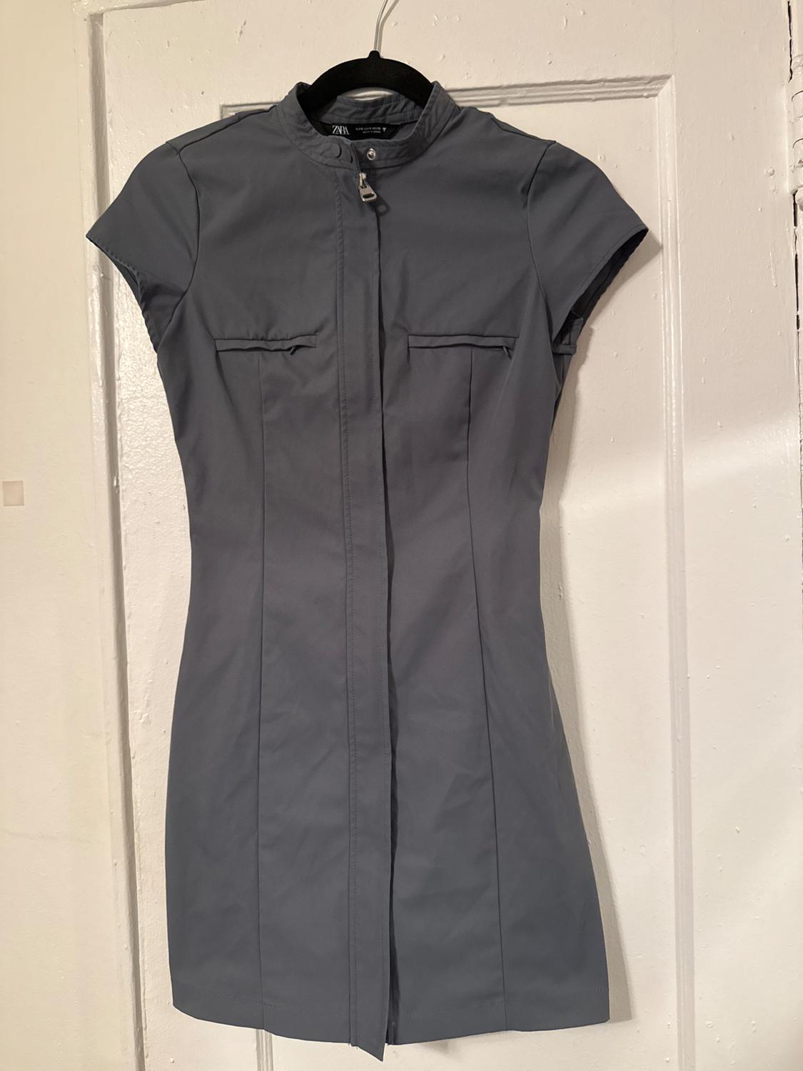 Short-sleeved gray dress hanging on a black hanger over a white door. Minimalist design with front closure.