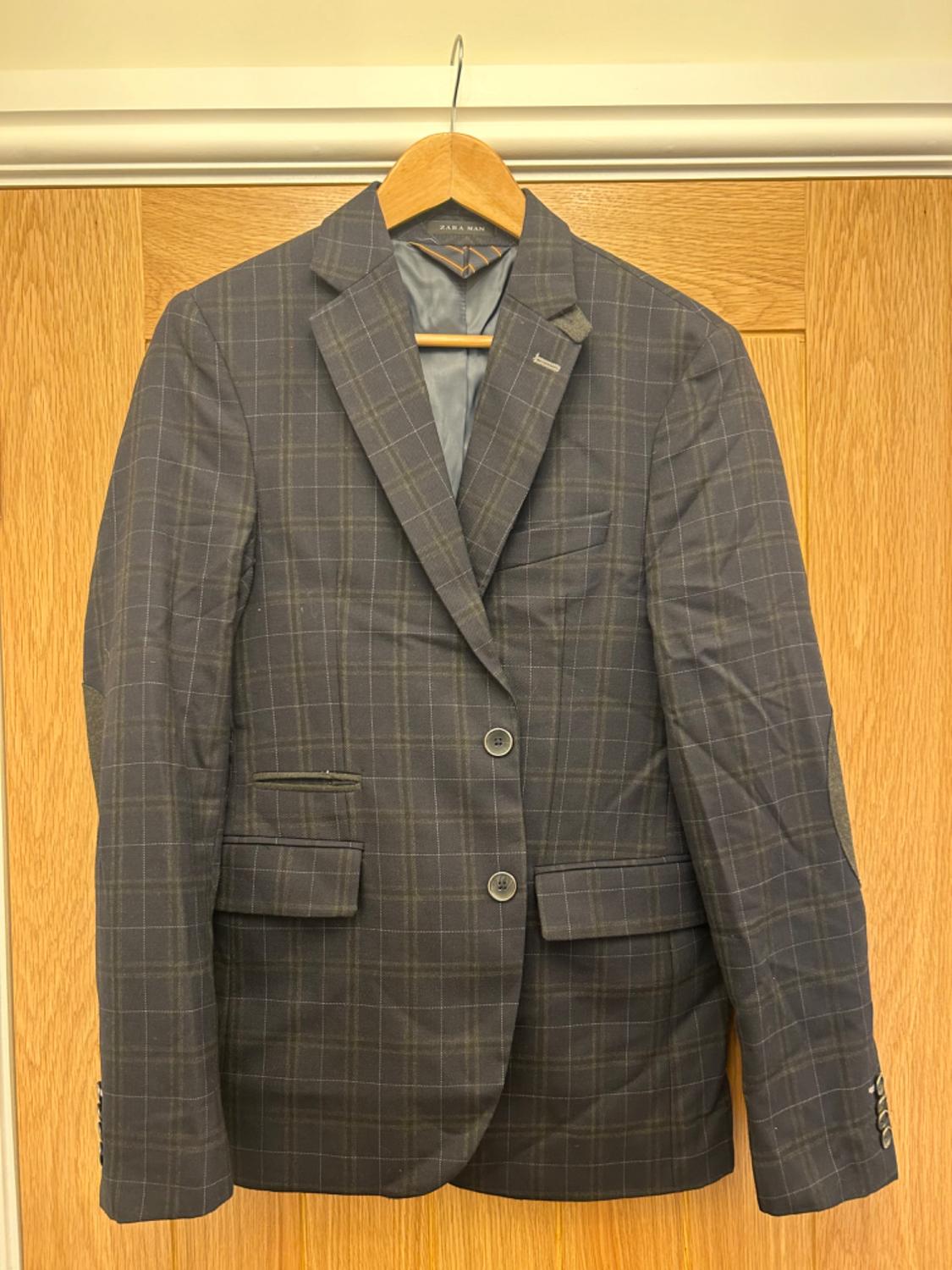 Front view of a dark checked jacket with lapels and flap pockets.