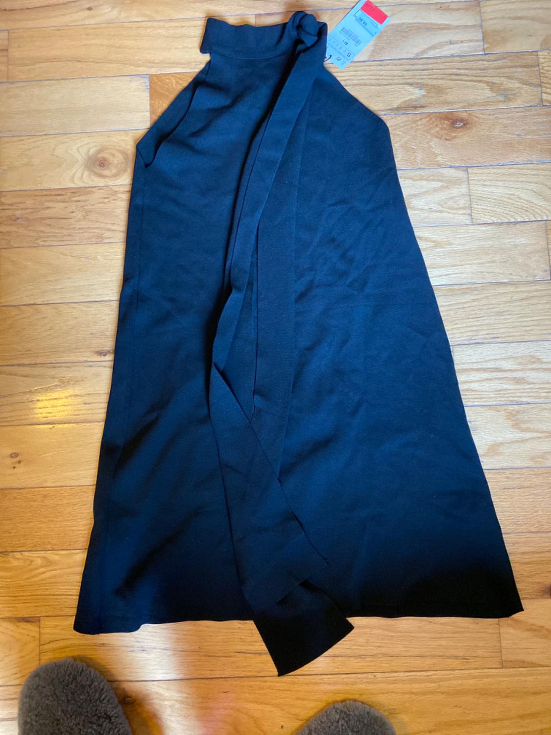 Front view of a black sleeveless dress with a high neck and a bow on the shoulder.