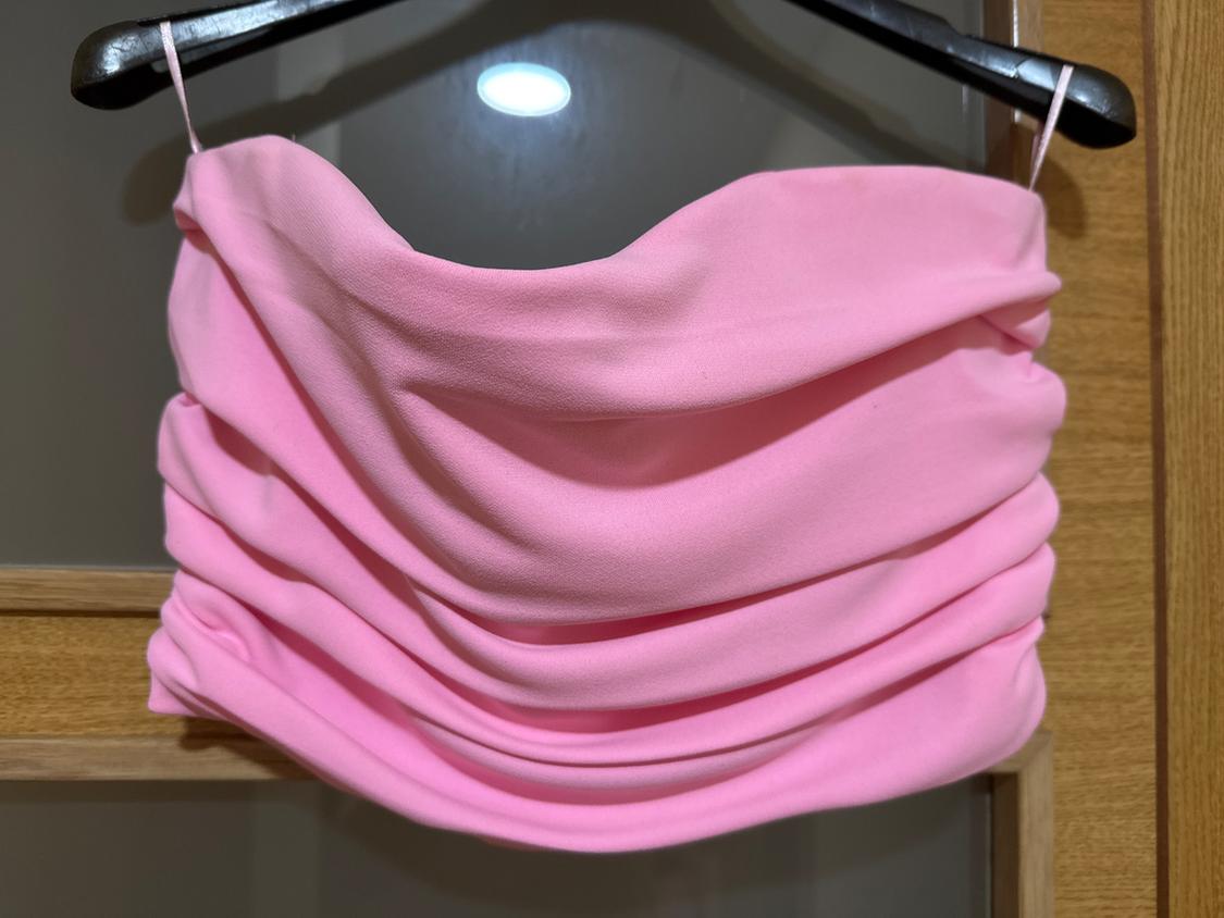Pink draped top hanging on a black hanger over a wooden door. The fabric has a soft, flowing look.