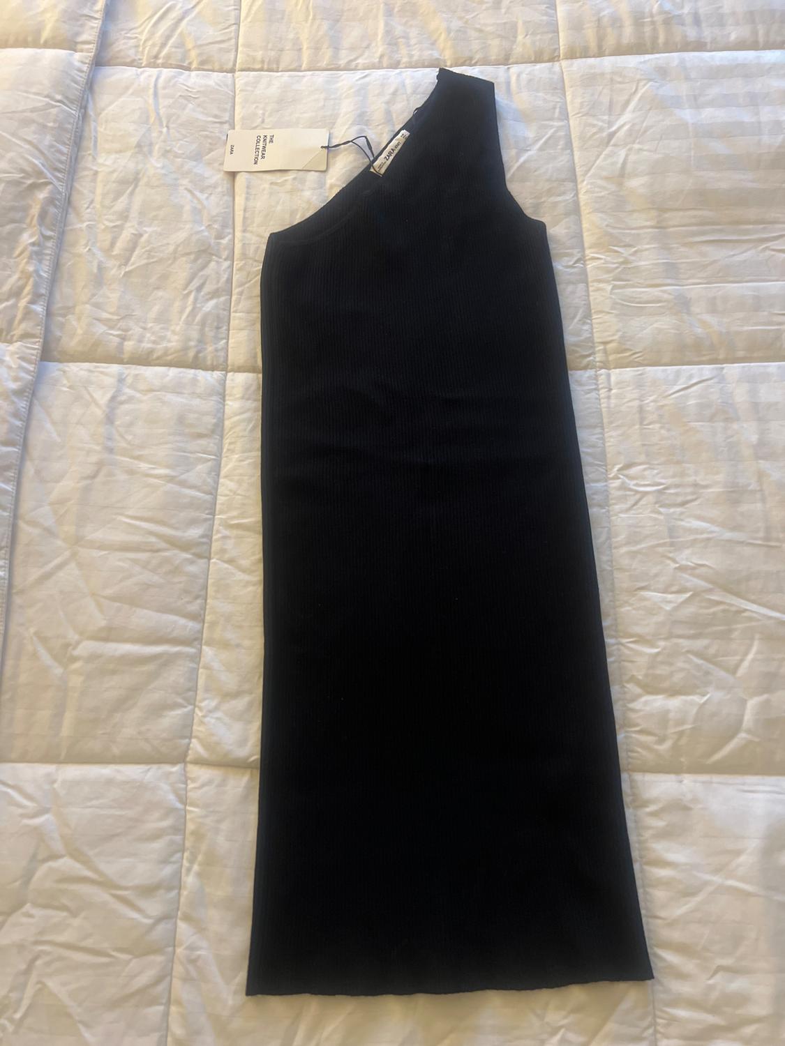 Front view of a black one-shoulder dress with a visible tag.