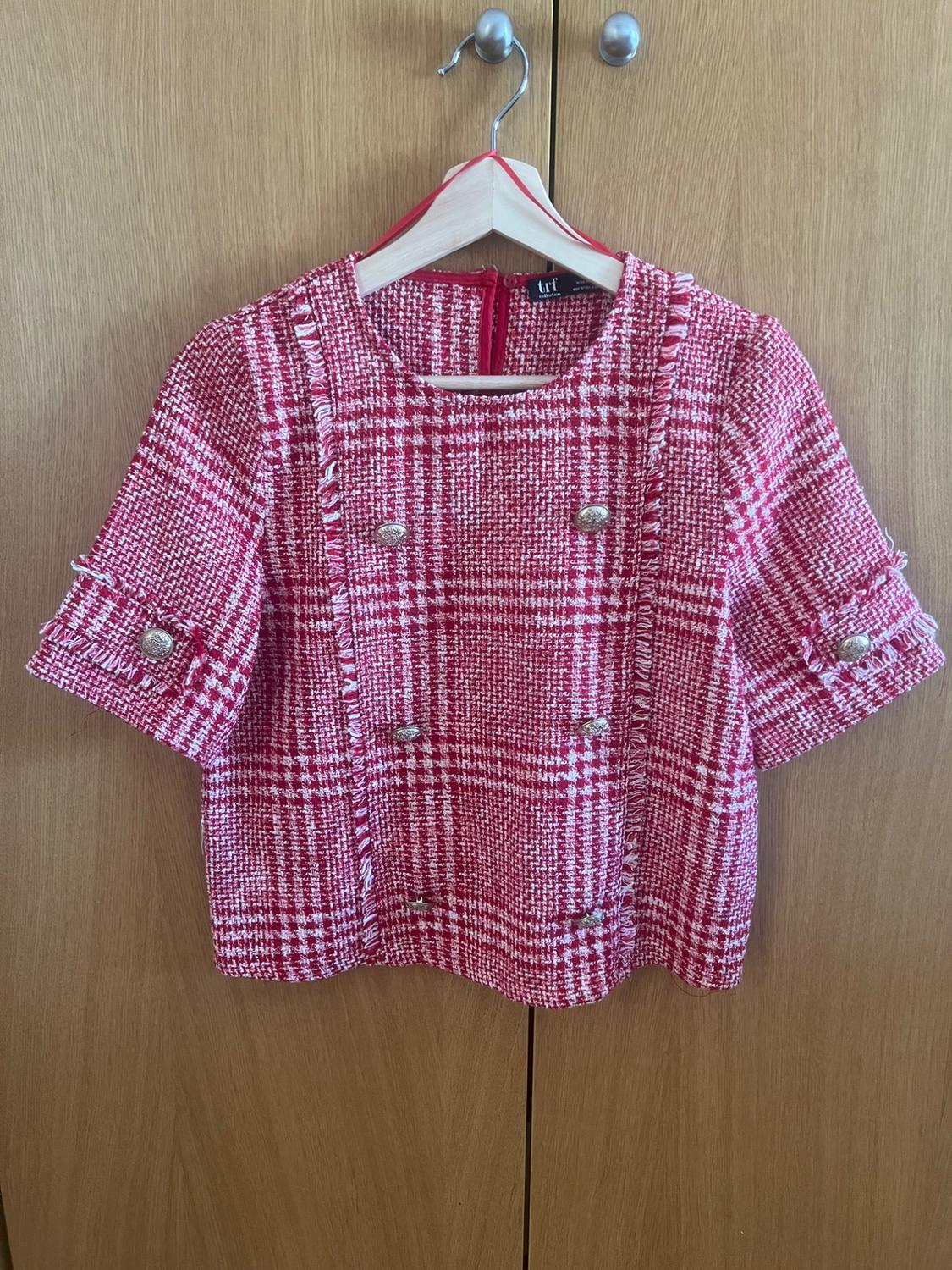 Red and white short-sleeved checked top with frayed edges and silver buttons, hanging against a wooden background. TRF label.