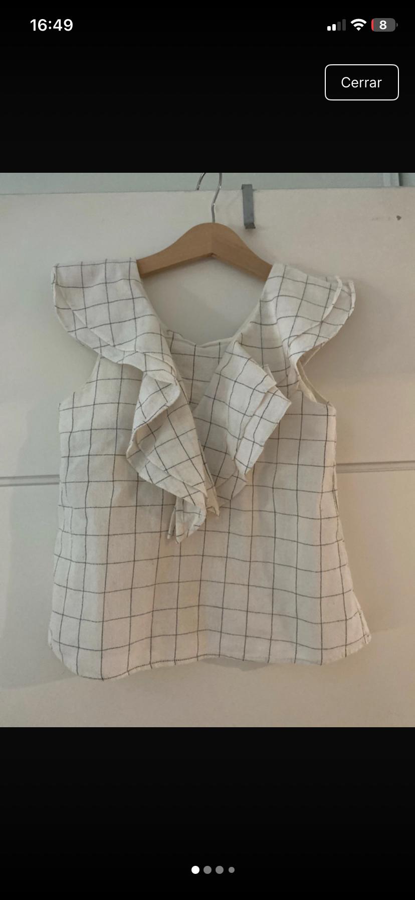 White blouse with black checks and ruffles on a wooden hanger over a white door. Text: 16:49 Close.