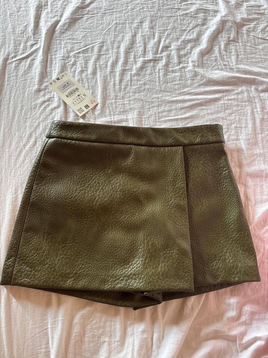 Olive green textured shorts on a white sheet, visible label with size and price details.