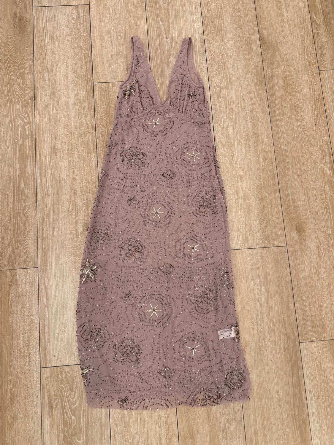 Mauve sleeveless maxi dress with a V-neck, decorated with floral and star-shaped beadwork. It is laid out on a wooden floor.