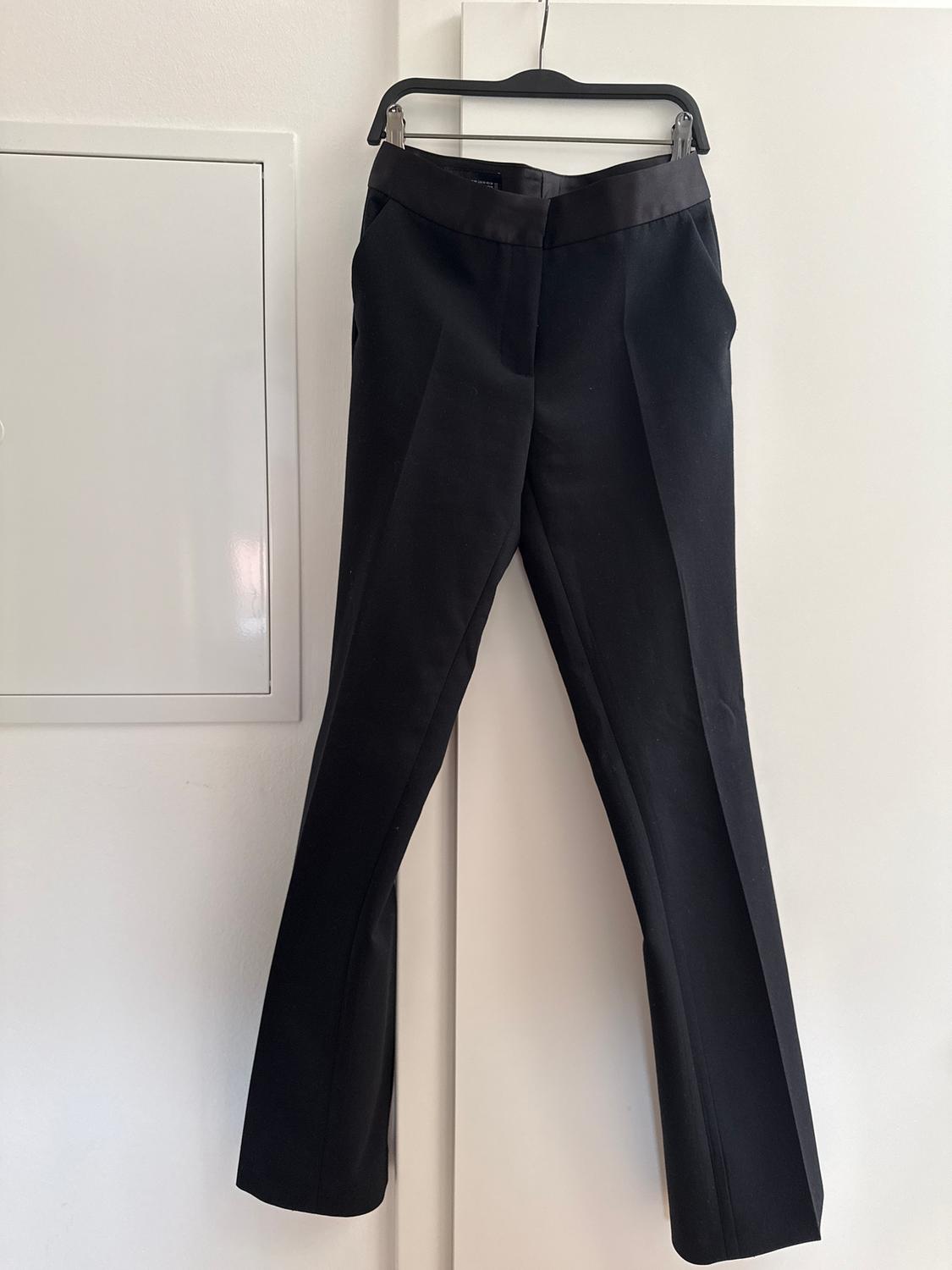 Black trousers hanging on a hanger over a white door. Minimalist and clean background.
