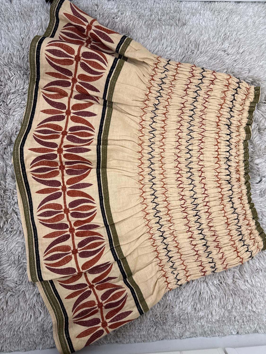 Beige skirt with ruched body, zigzag stitching and hem with brown leaf embroidery, on a grey rug.