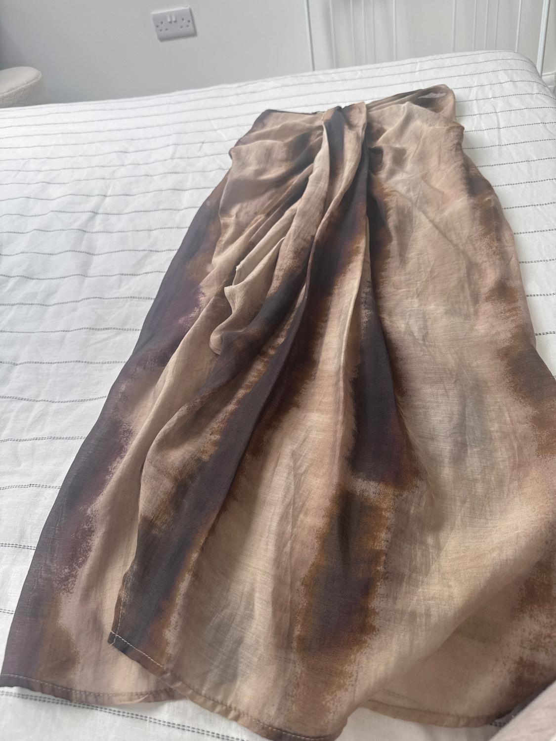 Long silk skirt in shades of brown and beige, with a gradient effect, placed on a bed with a striped white bedspread.