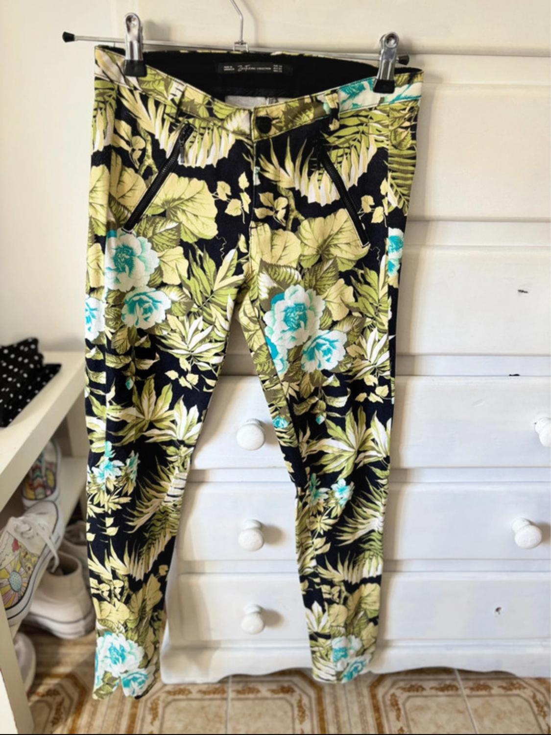 Front view of green and blue floral print trousers, with side zip pockets.