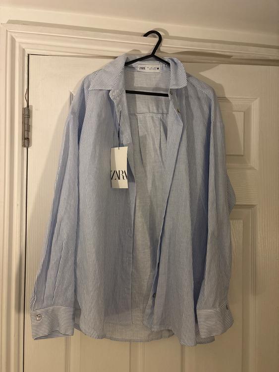 Blue and white striped shirt hanging on a black hanger over a white door. Visible tag with the text "ZARA".
