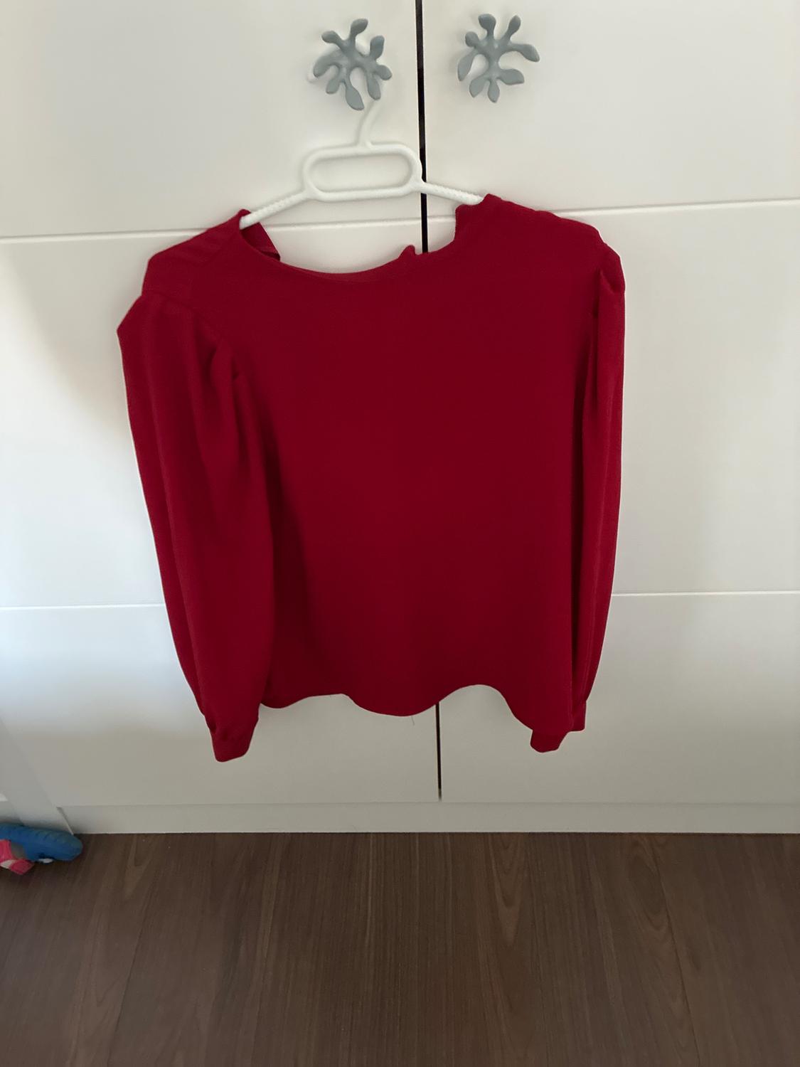 Red long-sleeved blouse with puffed shoulders, hanging on a white hanger in front of a white wardrobe.