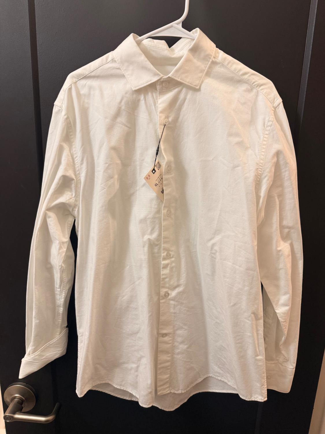 White long-sleeved shirt hanging on a white hanger over a dark door. Visible tag on the collar.