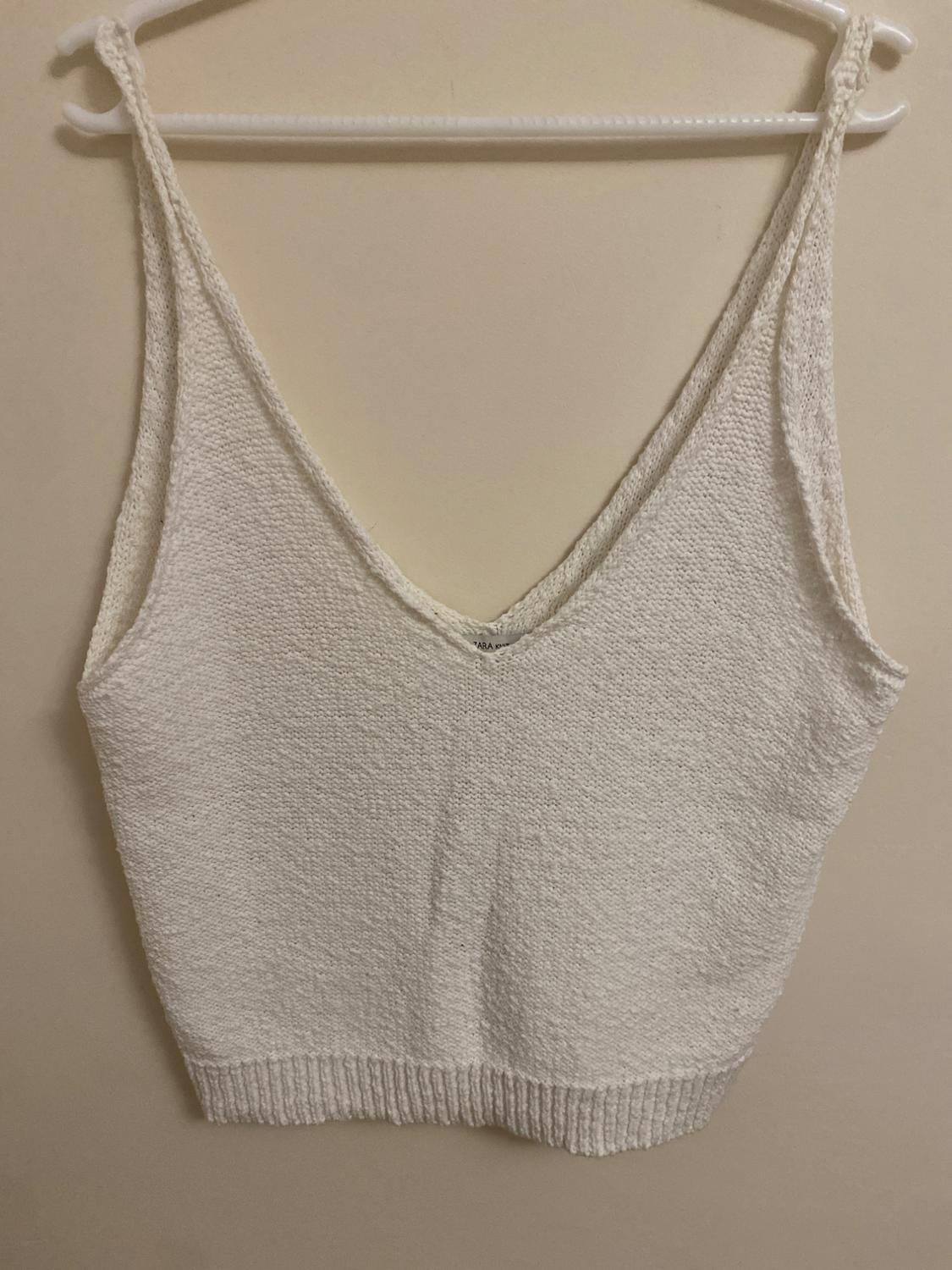 Front view of a white sleeveless top with a V-neck and a knitted texture.