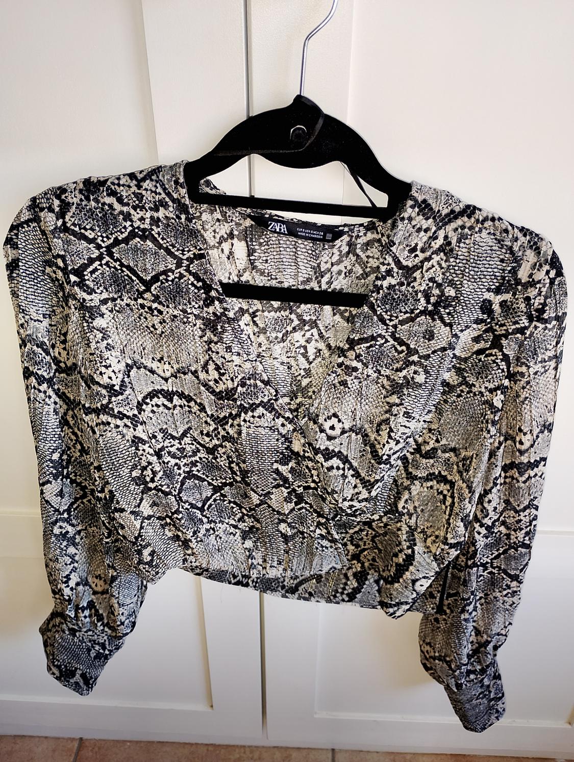 Long-sleeved blouse with a grey and black snake print, hanging on a black hanger in front of a white door.