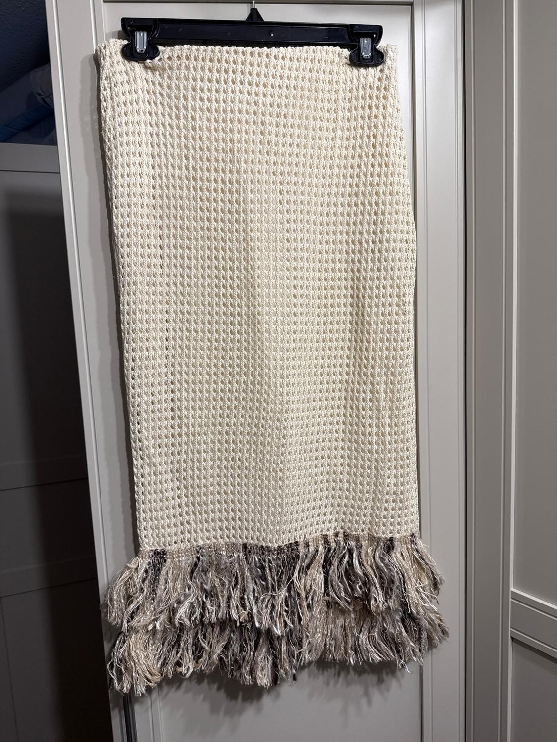 Beige knit skirt hanging on a black hanger, with fringe on the bottom hem, against a white closet background.