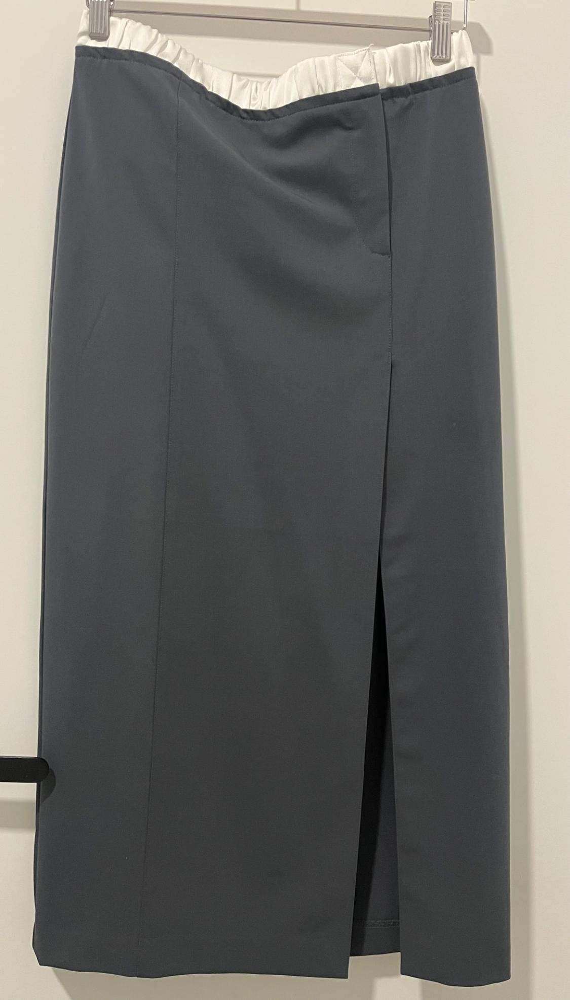 Grey skirt with white elasticated waistband and side slit, hanging on a hanger on a white background.