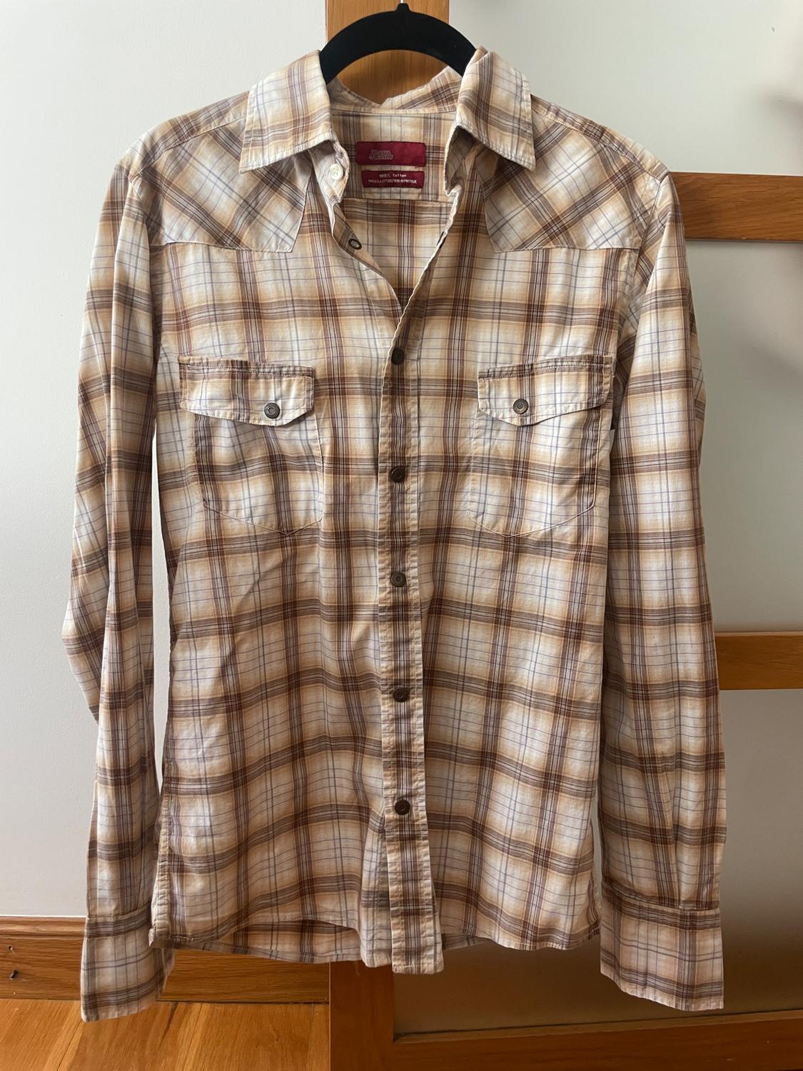 Brown and white checked long-sleeved shirt with chest pockets. It is hanging on a black hanger against a light background.