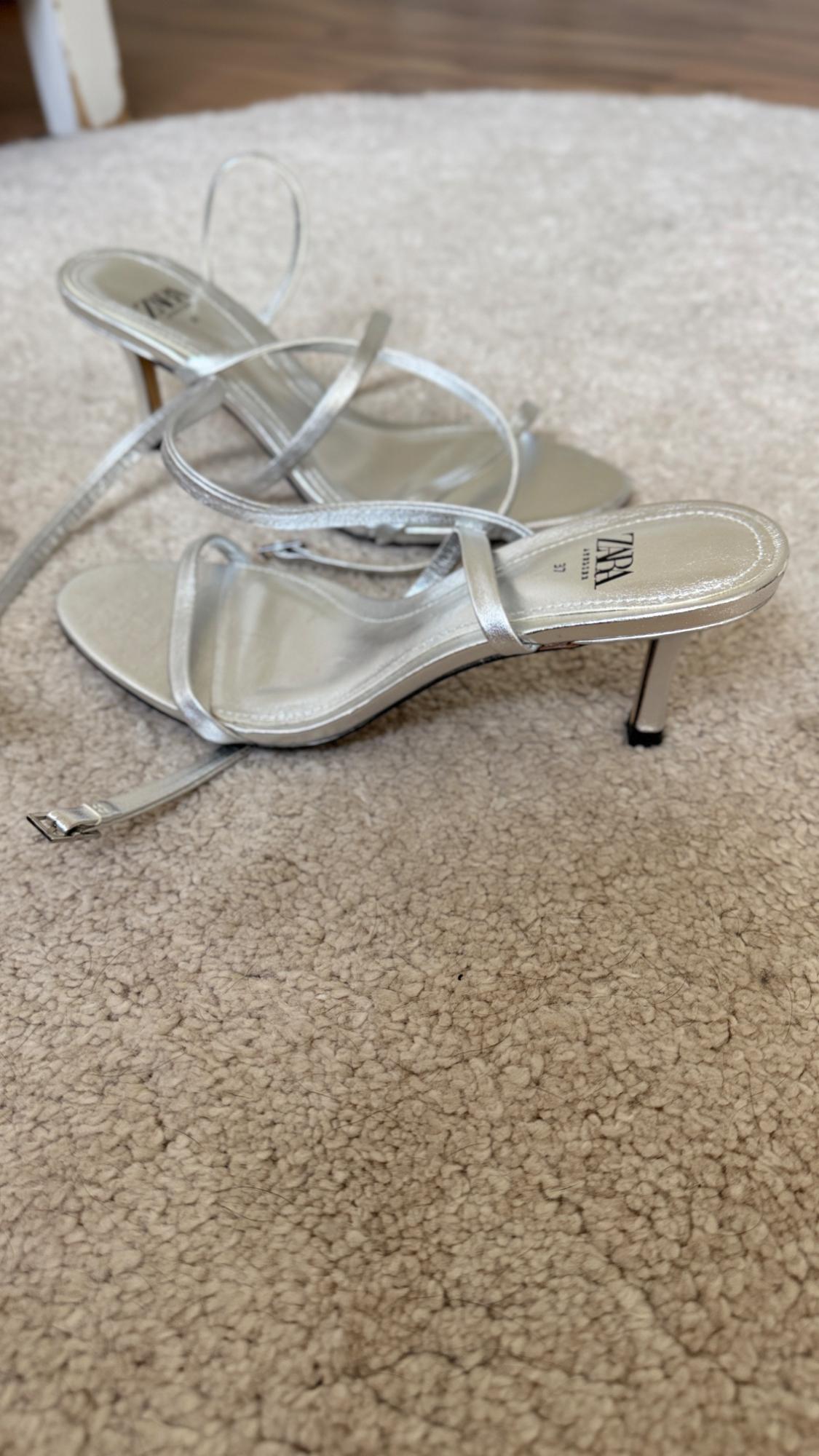 Pair of silver strappy heeled sandals on a beige rug. The insole reads ZARA 37.