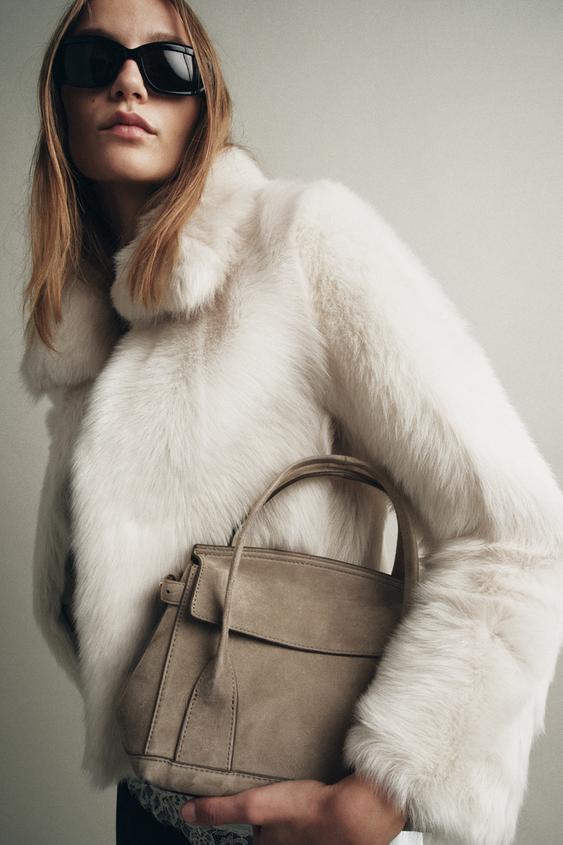 Střední plán šedé tašky s dvojitým uchem a klopou. Viditelný bílý kabát.