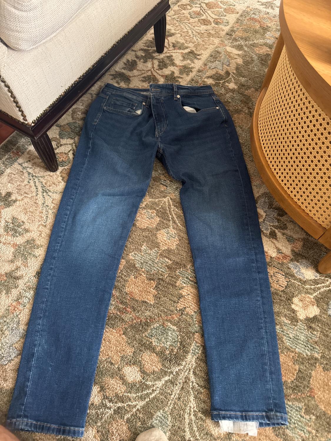 Blue jeans laid out on a floral-patterned rug, next to a sofa and a wooden table.