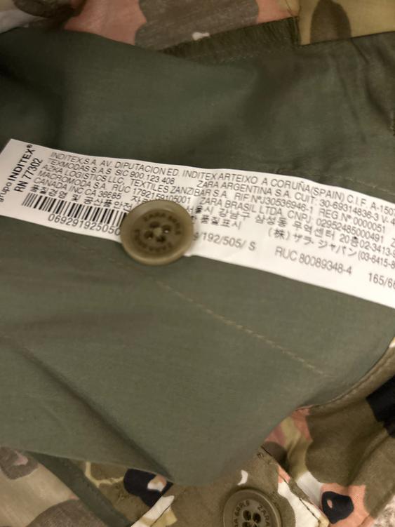 Clothing label with Inditex manufacturing and distribution text, on green fabric with brown and pink camouflage print.