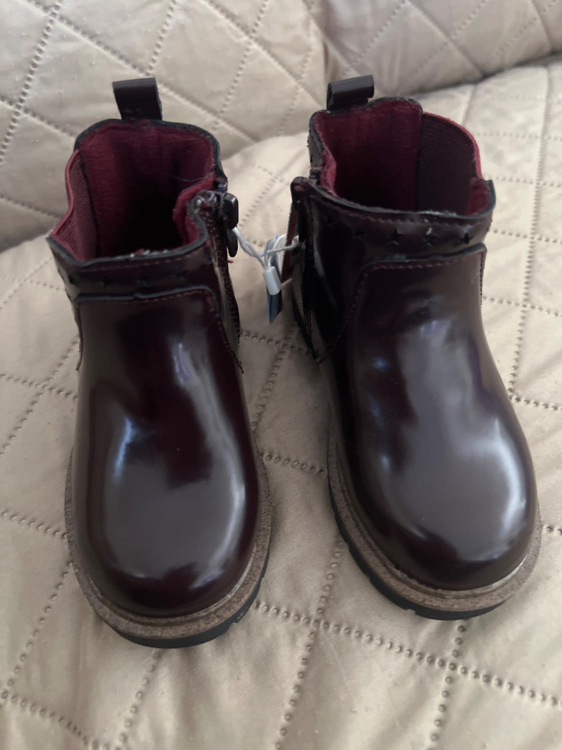 Dark brown patent leather boots with a burgundy interior on a beige quilted comforter.