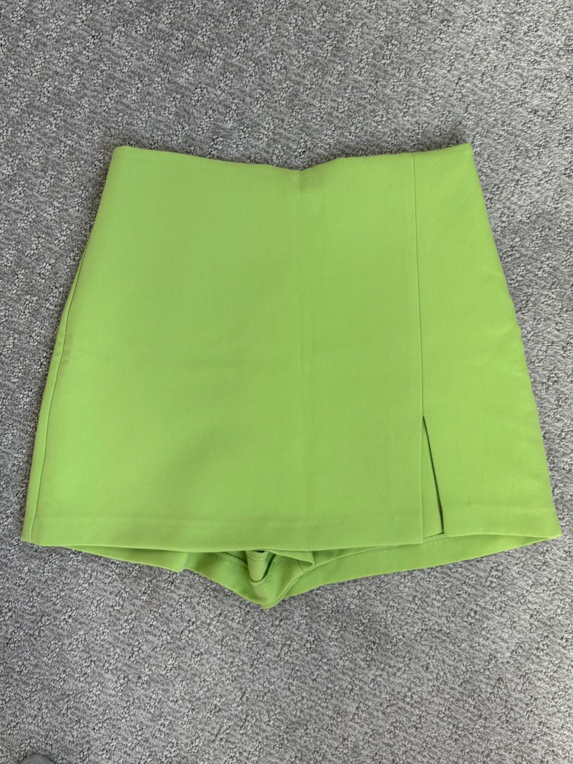 Lime green skirted pants with a side slit, arranged on a gray rug.