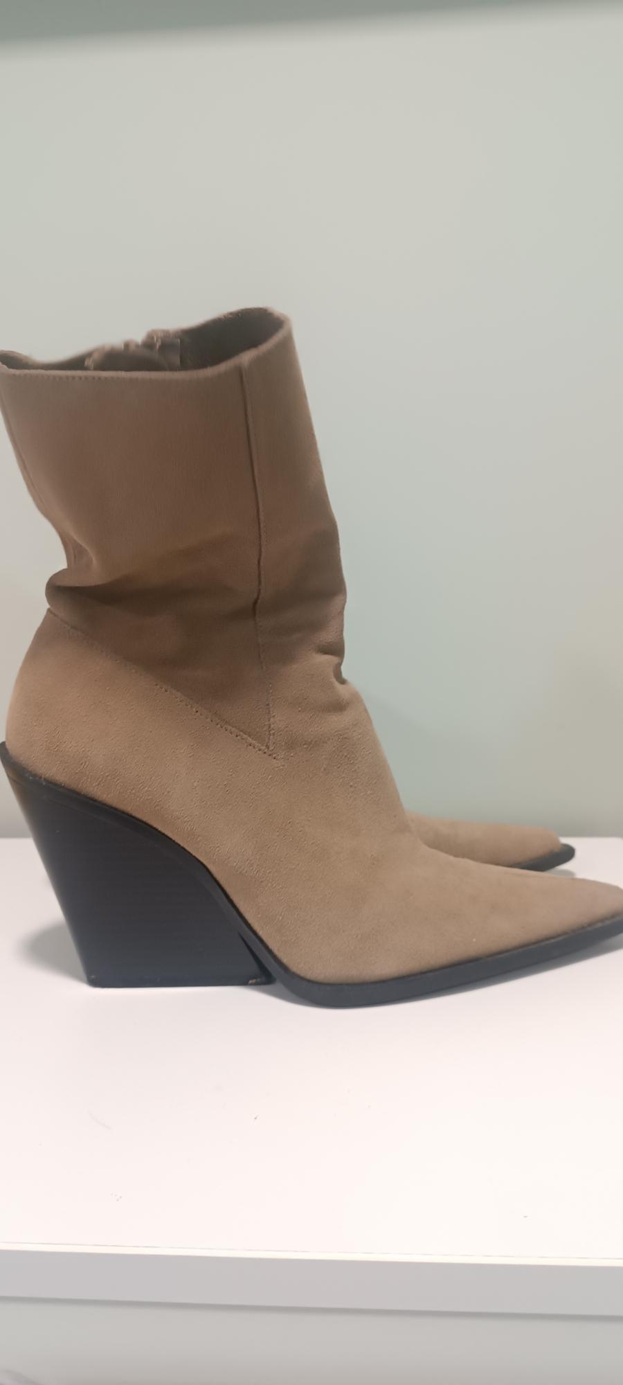 Beige high-heeled boots with a pointed toe, on a white surface and light background.