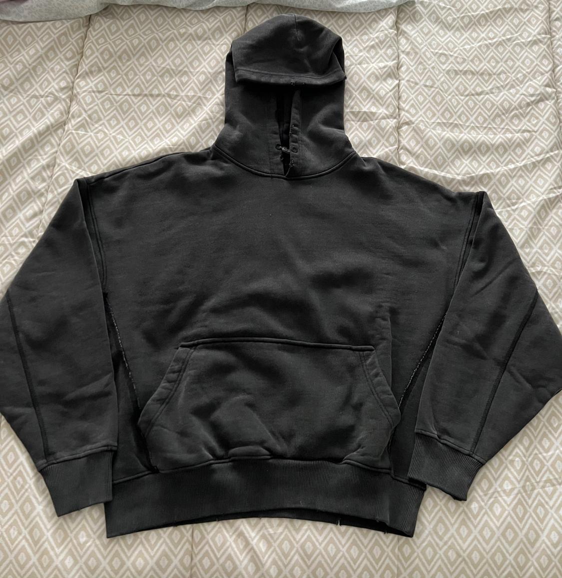 Black hoodie with a front pocket, placed on a quilt with a geometric pattern in light tones.