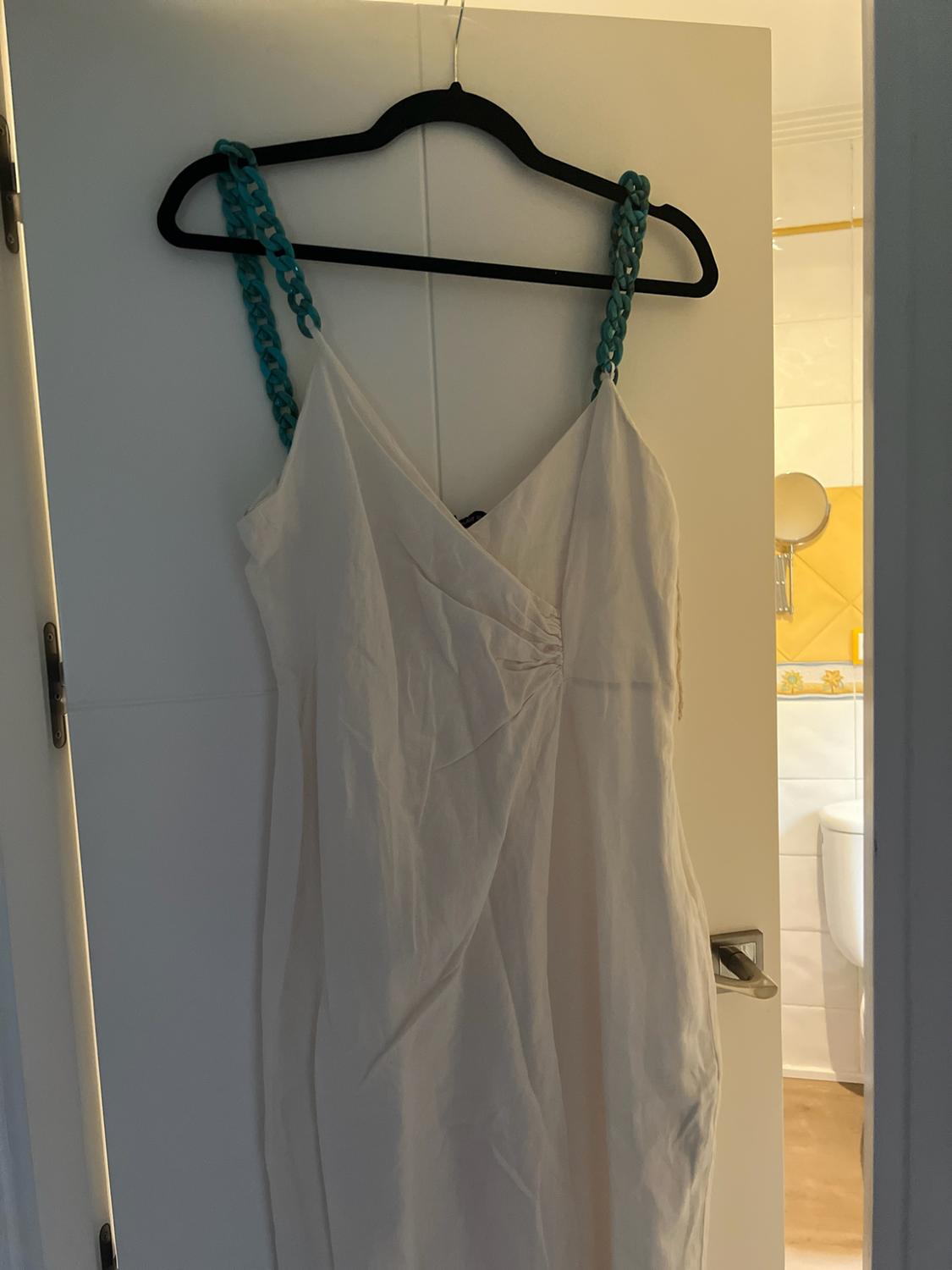White dress with turquoise link straps on a black hanger, hanging from a white door. Bathroom in the background.