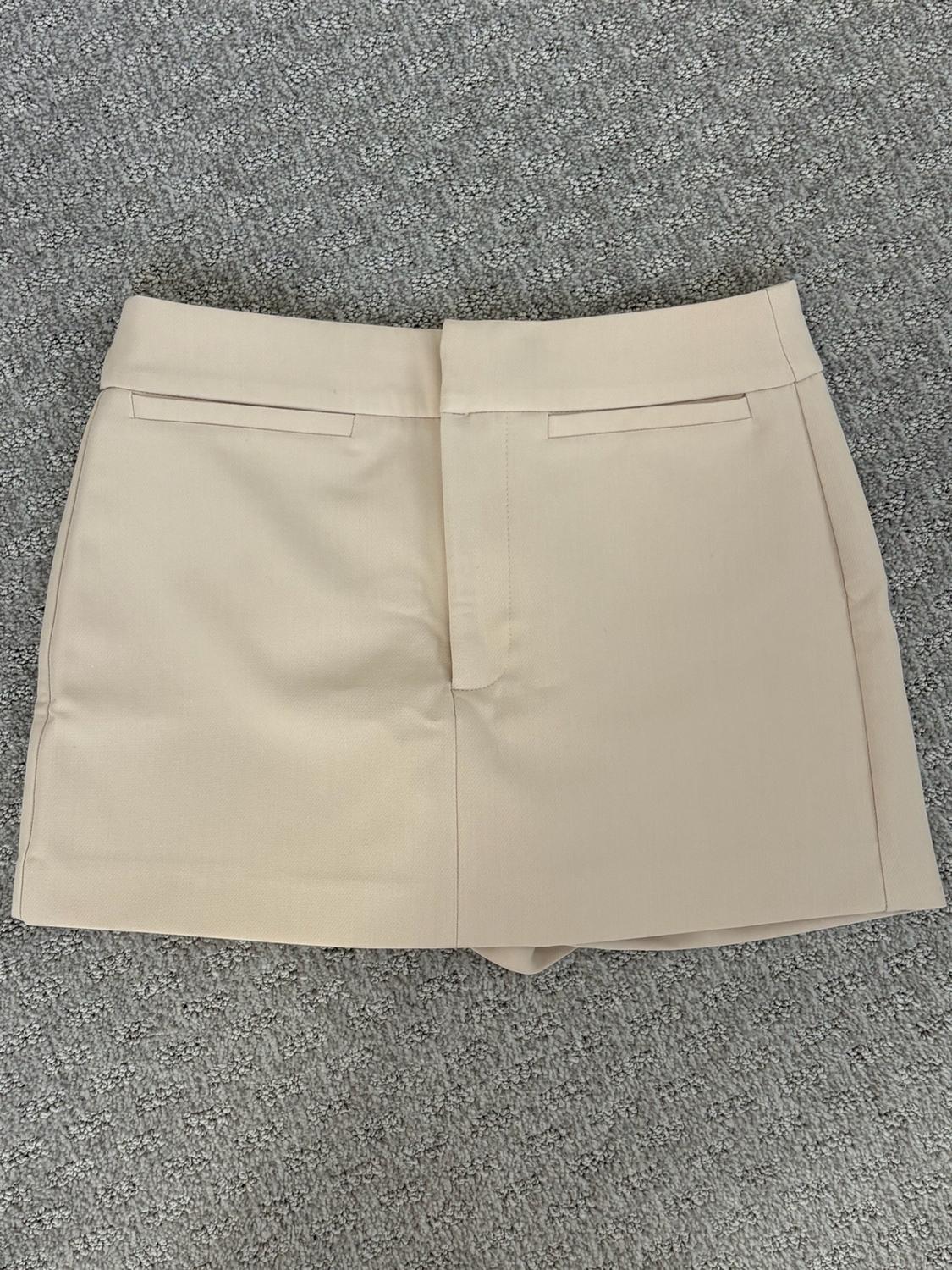 Light beige short skirt with a concealed front zipper and pockets, photographed in a flat lay on a gray rug.