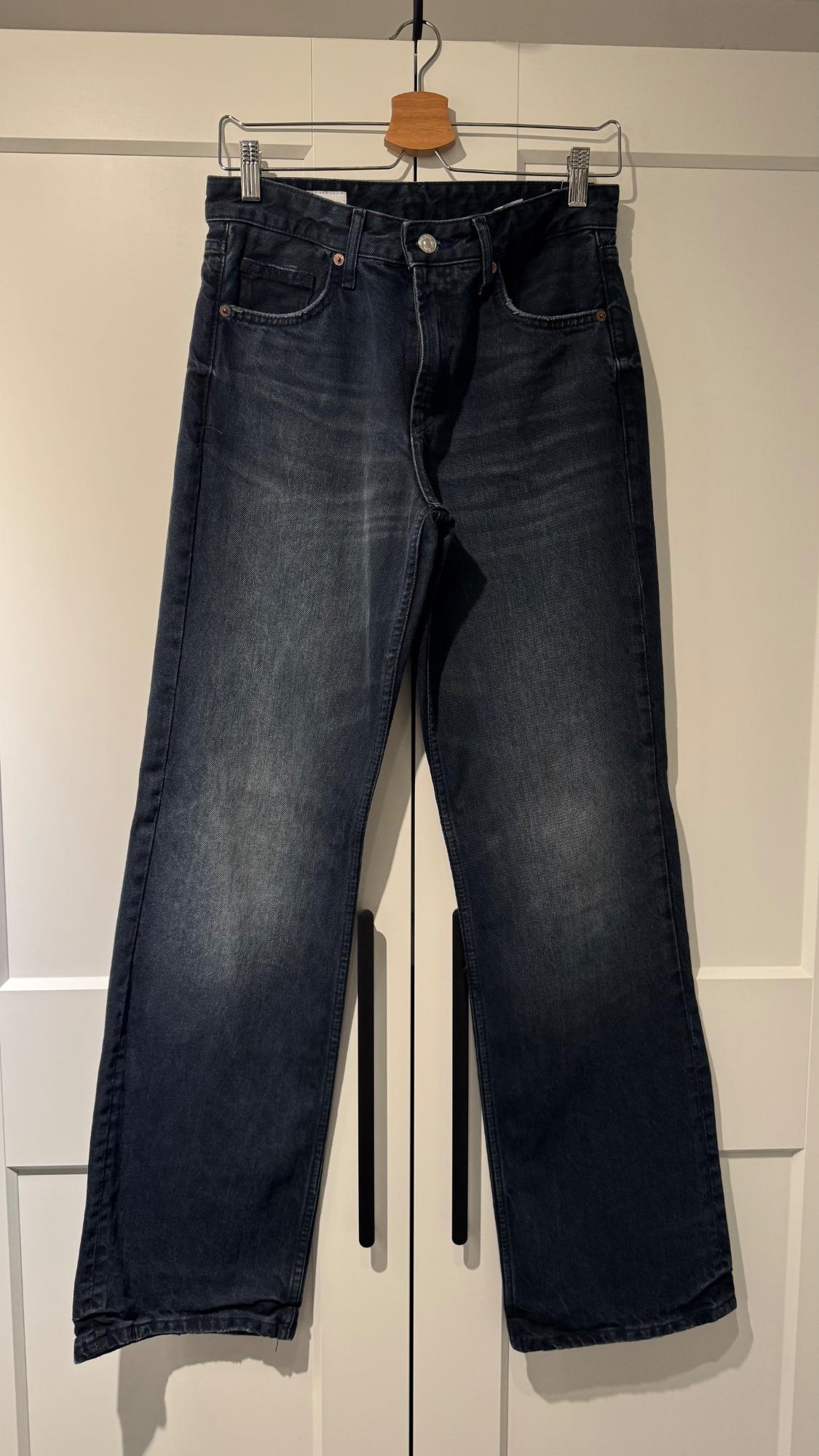 Dark denim jeans hanging on a wooden hanger against a backdrop of white doors with black handles.