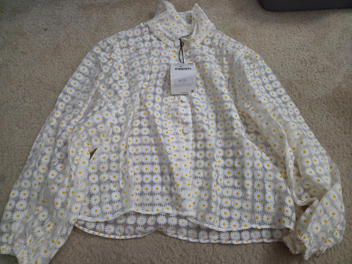 White blouse with yellow daisy print on a beige rug. Visible tag with price of 49.00.