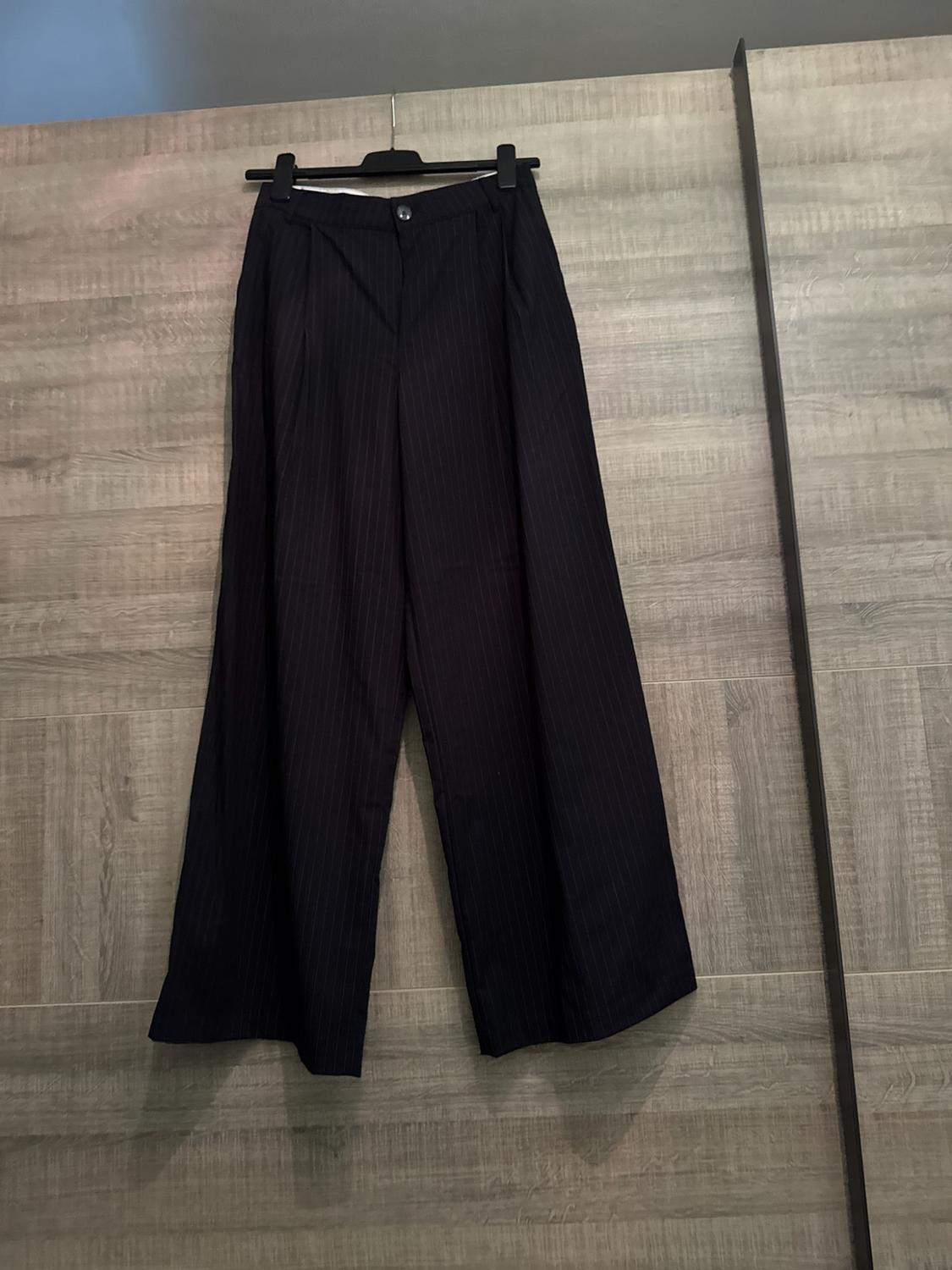 Dark wide-leg pinstripe trousers hanging on a black hanger in a wooden wardrobe. Casual and relaxed style.