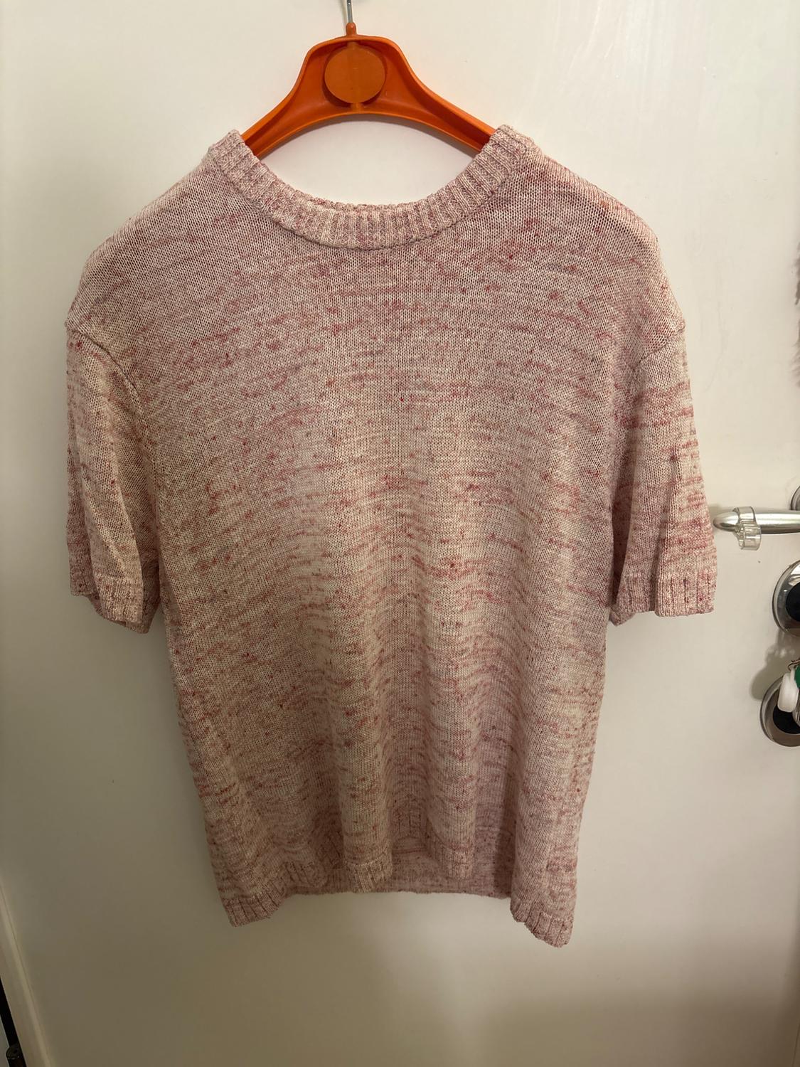 Marl knit jumper in shades of pink hanging on an orange coat hanger over a white door.