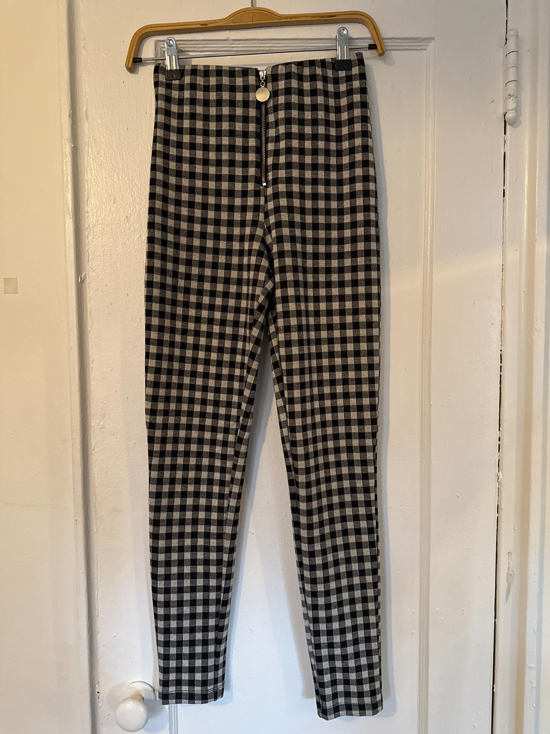 Black and white plaid pants hanging on a wooden hanger over a white door. Zipper and button visible.