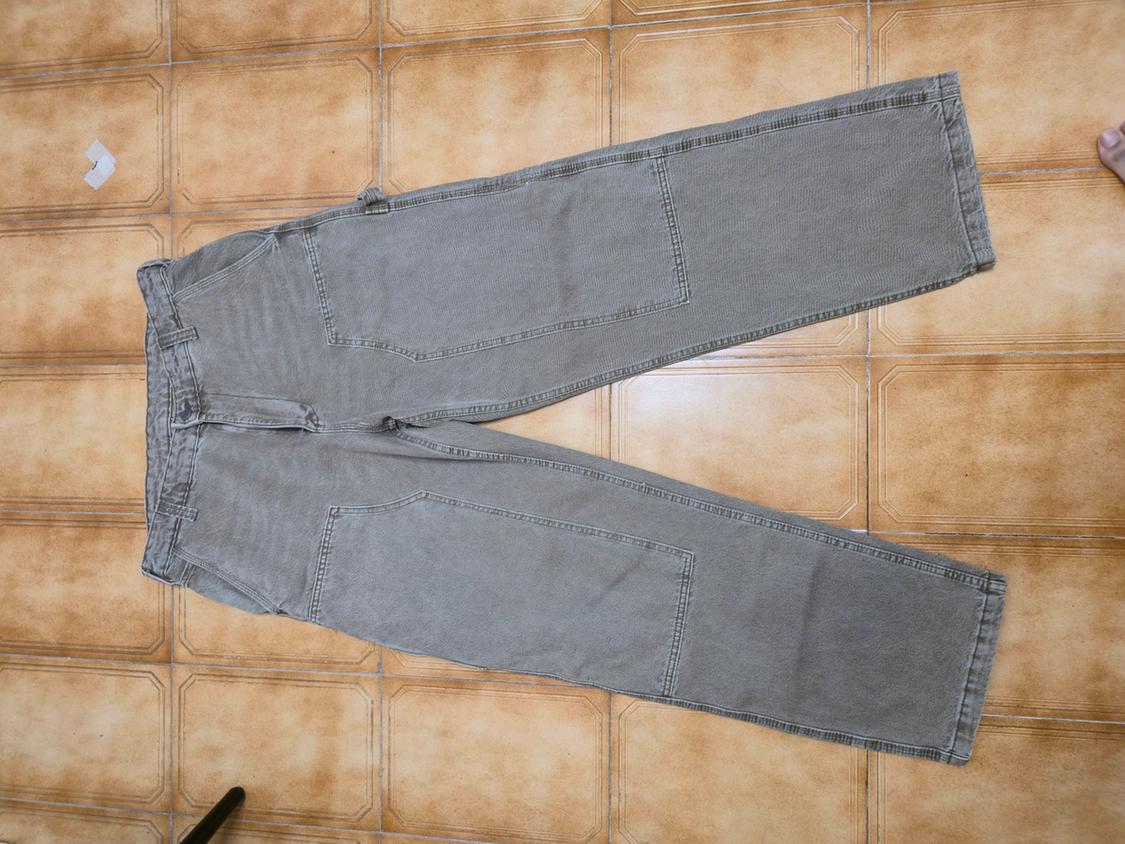 Grey denim trousers with large pockets, placed on a brown tiled floor.