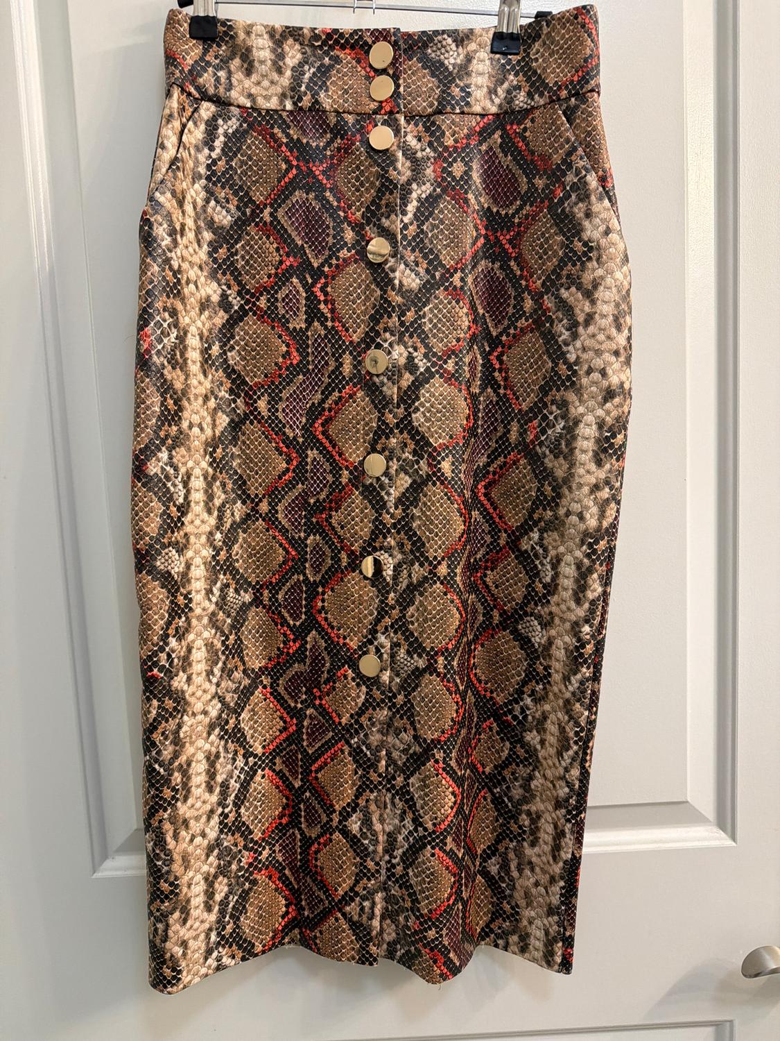Snake print skirt in brown and red tones, with gold buttons on the front, hanging on a white door.