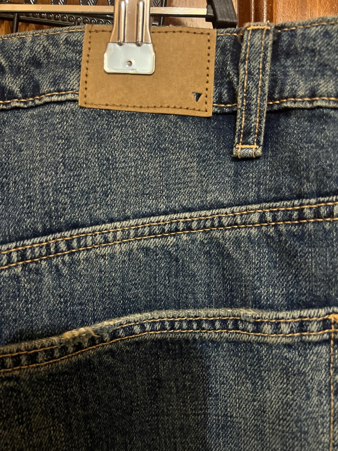 Detail of the back of a pair of blue jeans on a hanger, showing the brown label on the waistband and the double stitching.