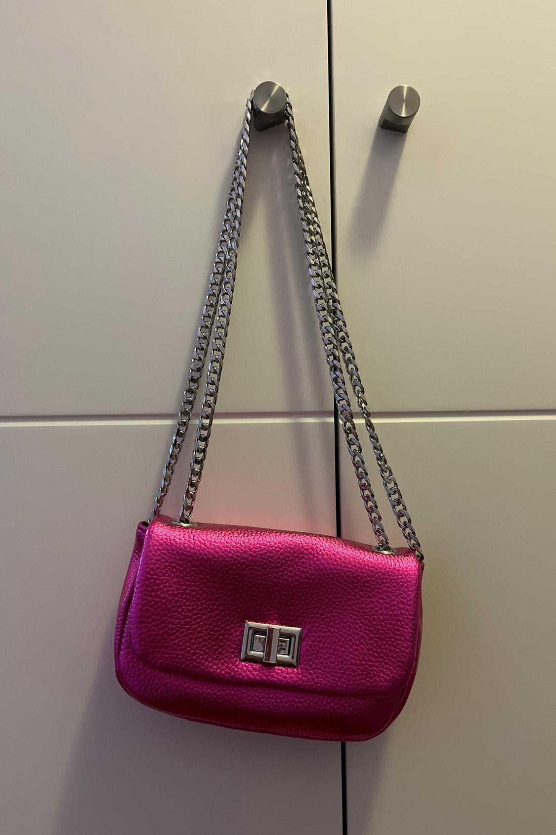 Pink handbag with metal chain and buckle fastening, hanging on a hook.