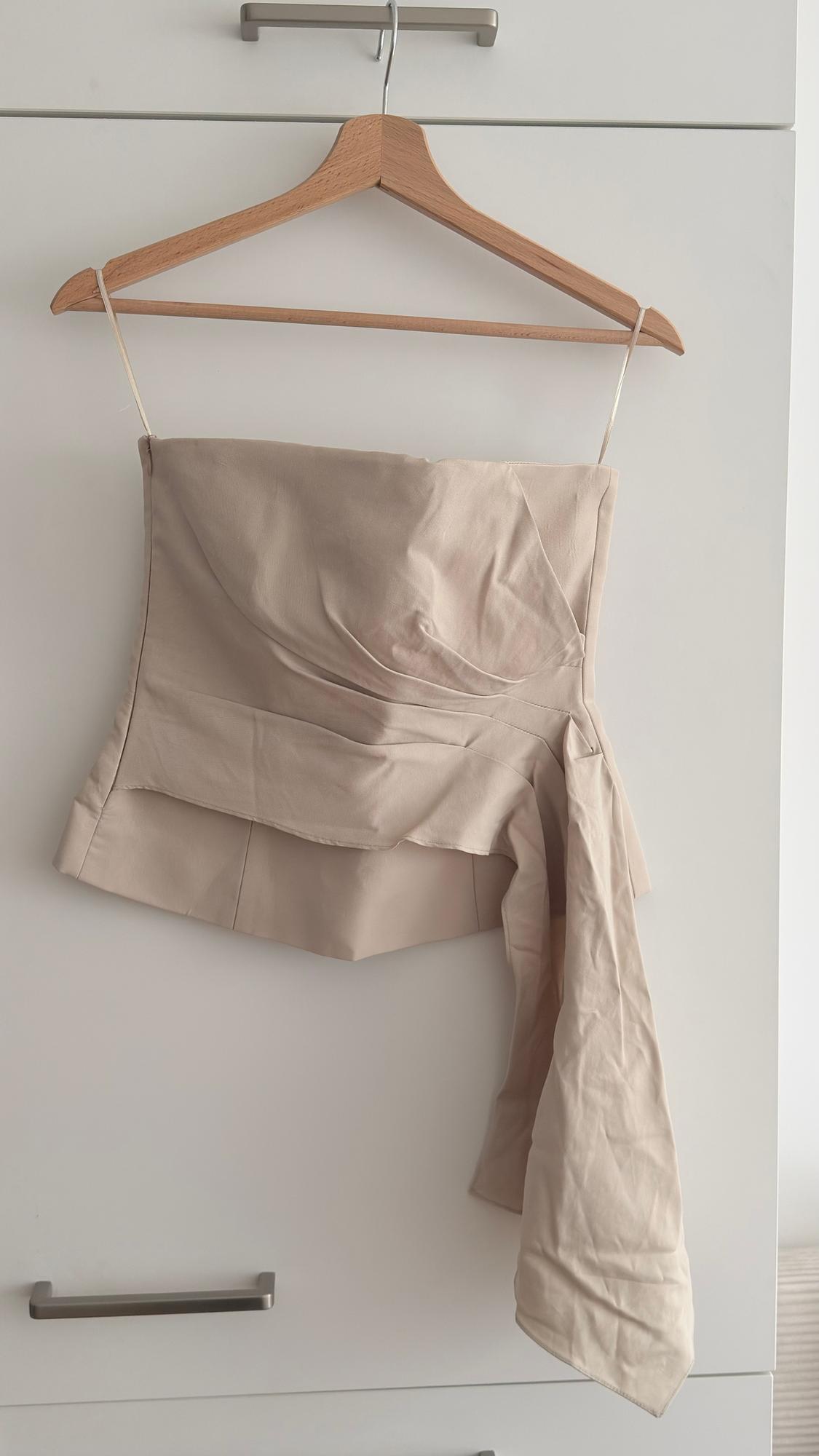 Top beige strapless hanging on a wooden hanger against a white background. The fabric has a draped design.
