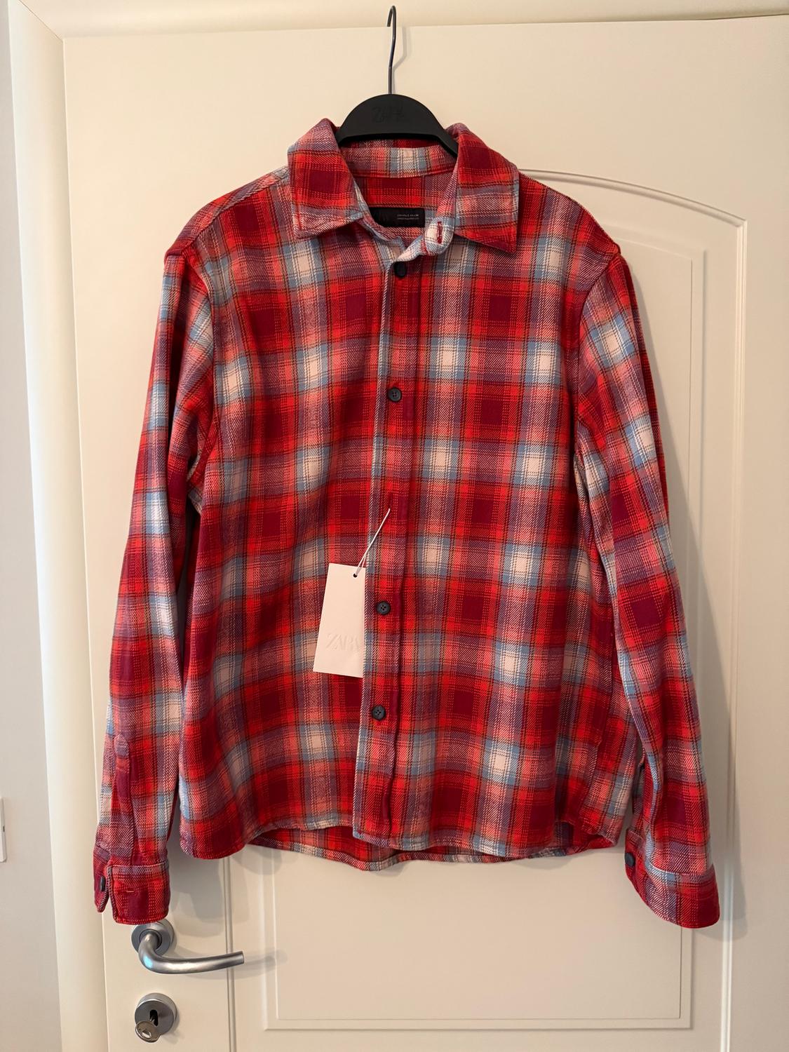 Red and grey checked shirt hanging on a white door, with visible tag.