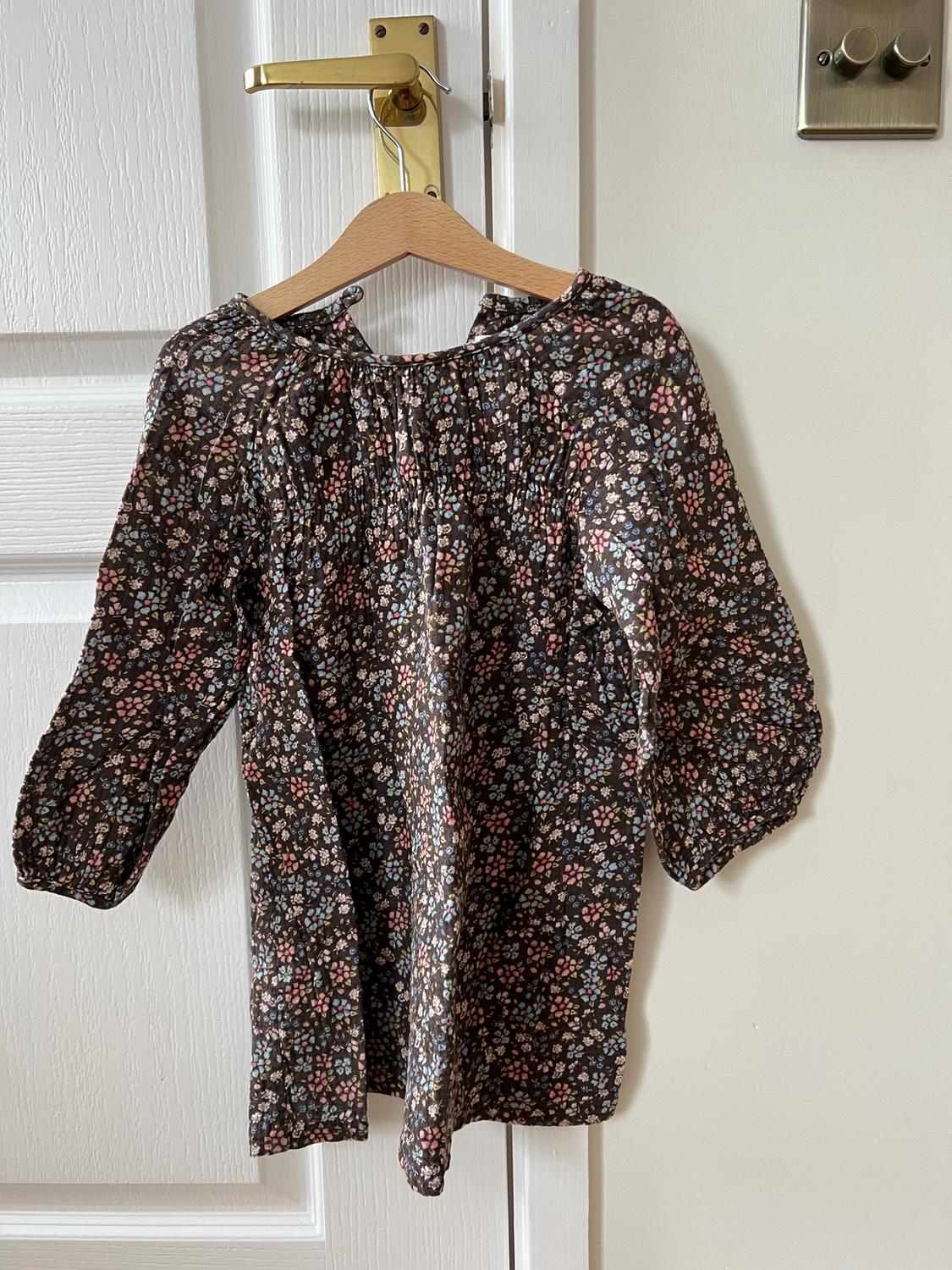 Long-sleeved blouse with a dark floral print, hanging on a wooden hanger over a white door.