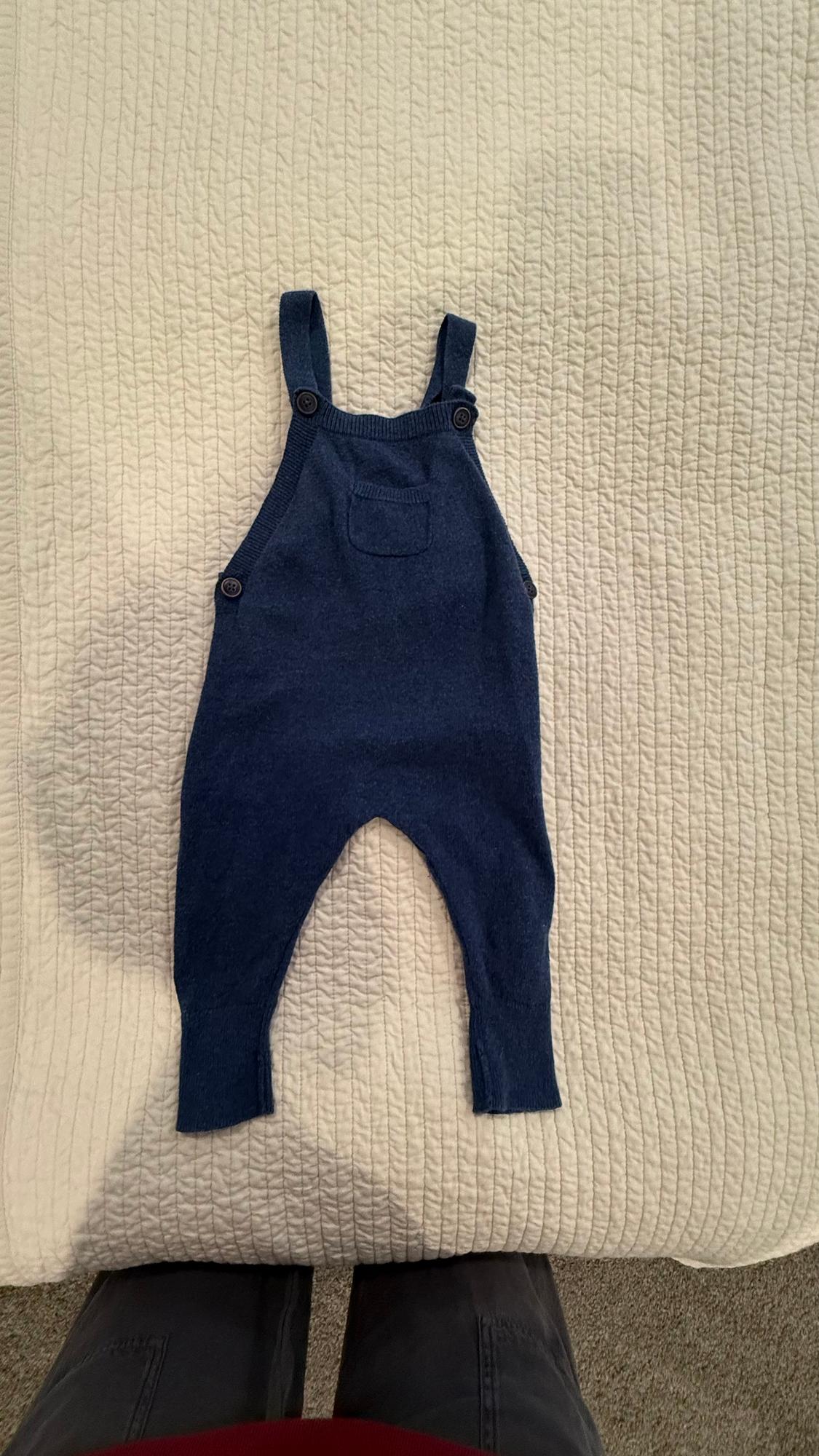 Baby's blue dungarees with straps and buttons, on a quilted white bedspread. Lower part of legs visible.