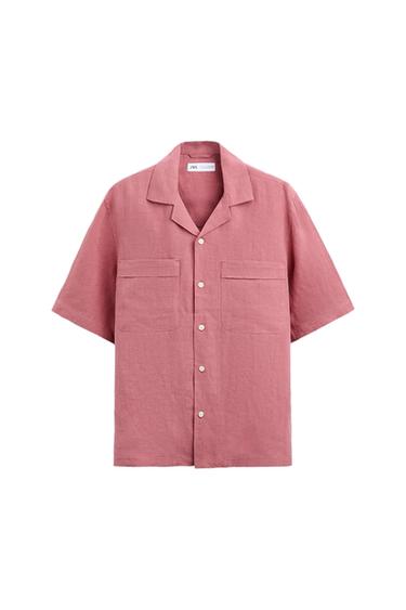 Pink short-sleeved shirt with white buttons and two front pockets. Visible label on the collar. White background.