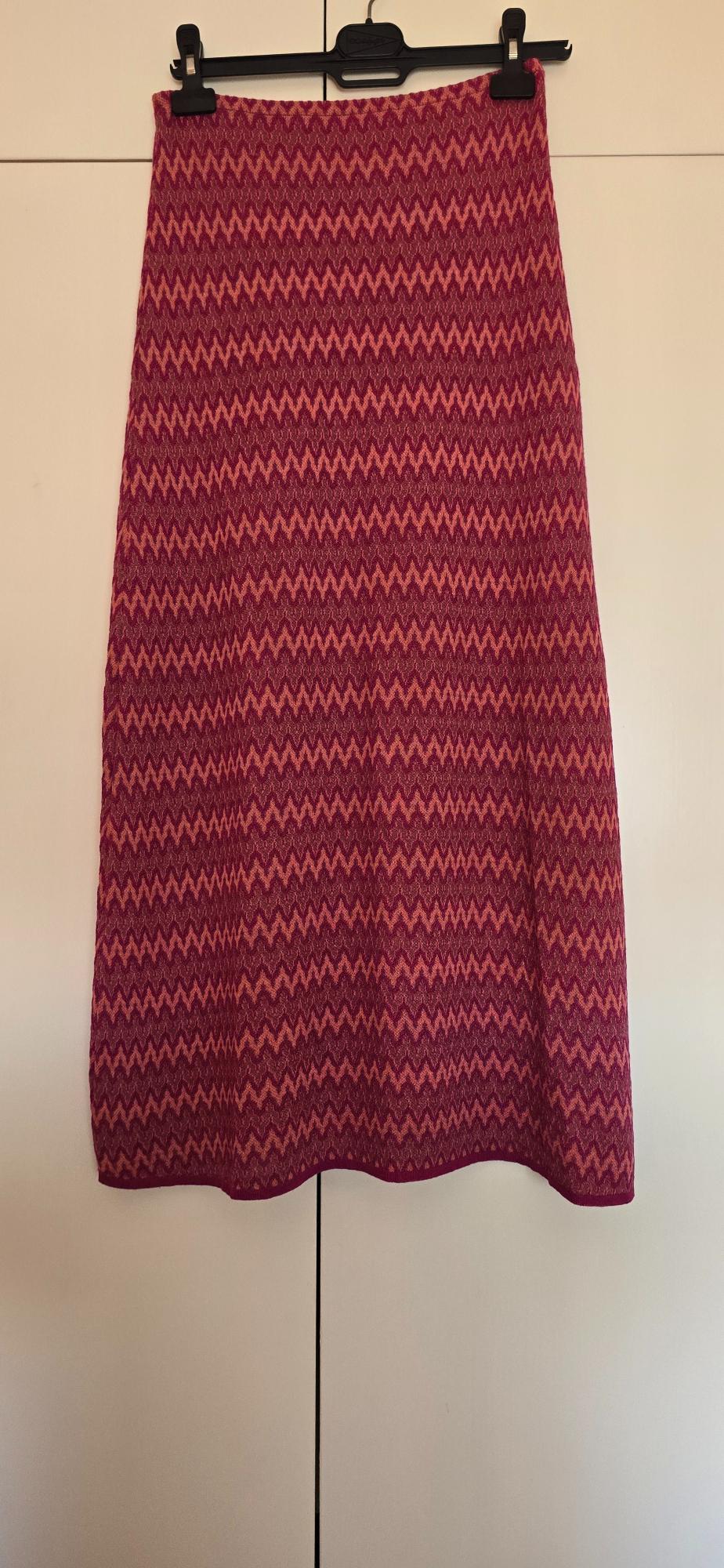 Fuchsia and orange zigzag-patterned knitted maxi skirt, hanging on a black hanger against a white wardrobe background.