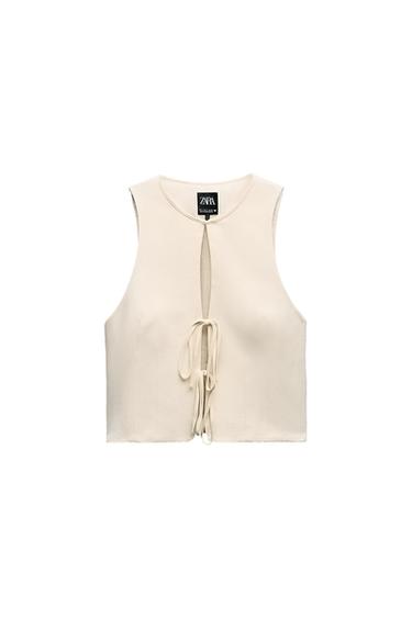 Front view of a sleeveless beige vest with an opening and tie at the chest.