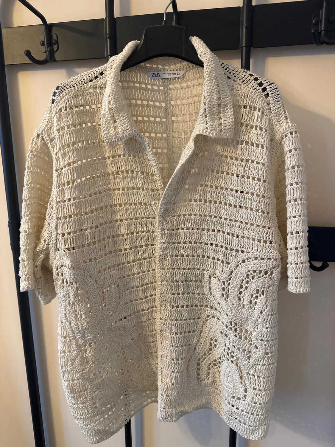 Beige crochet shirt hanging on a black hanger, with floral pattern design and short sleeves. Visible tag: Zara.