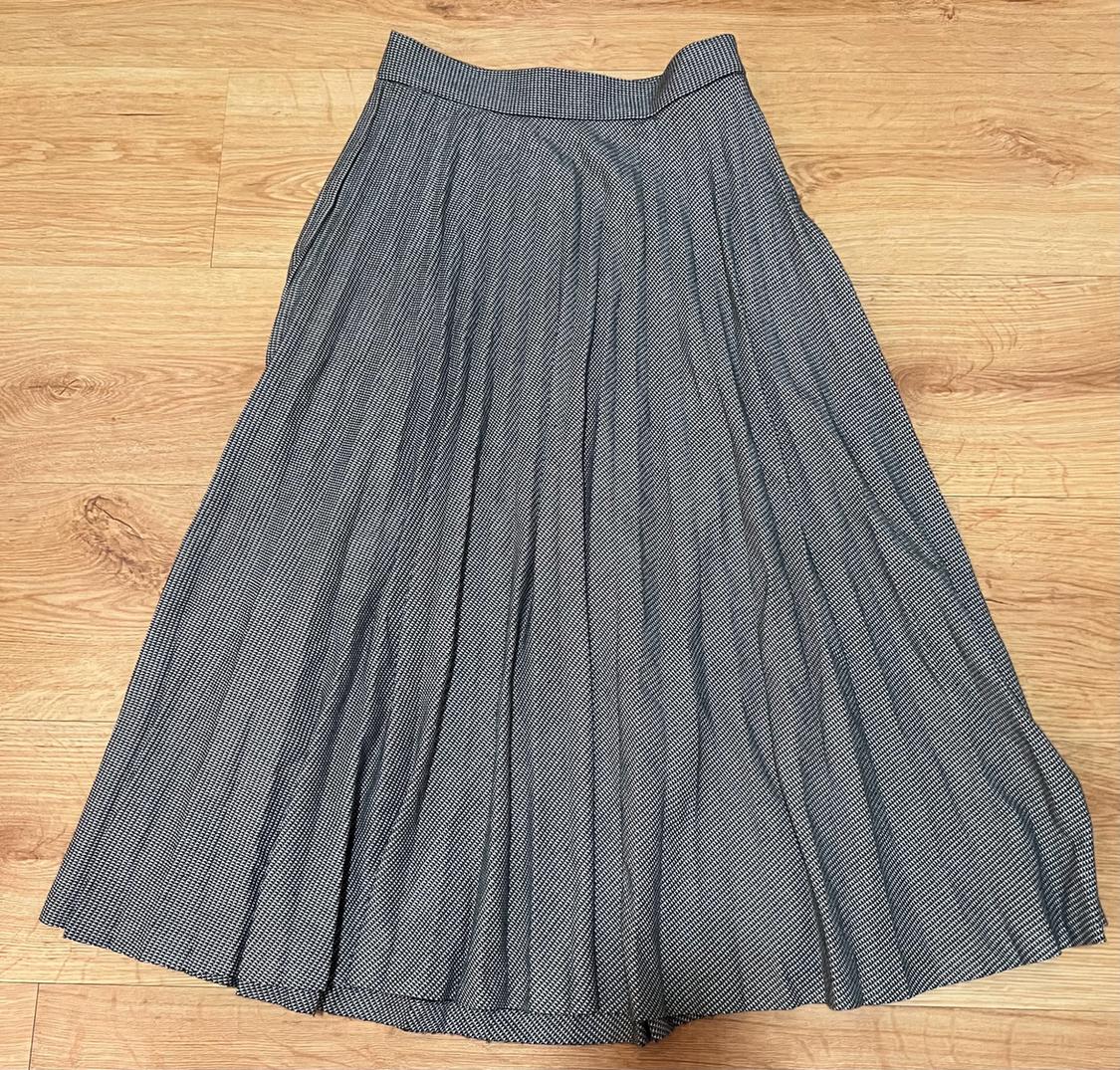 Long pleated skirt with a small black and white check print, laid out on a light wood floor.
